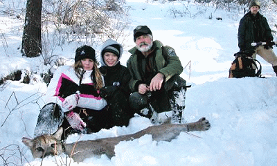 Project Cat crew in the field. Two young female students with Gary Koehler in snow gear crouching over a tranquilized cougar. Teacher in background looking on.