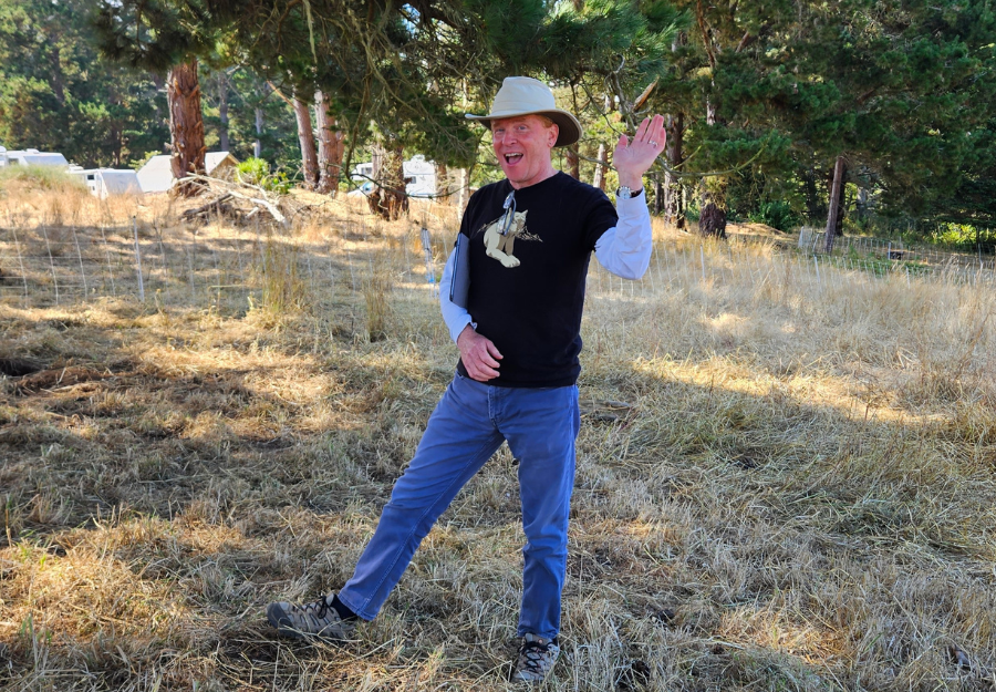 Man wearing jaunty hat, mountain lion t-shirt and jeans, waving happily